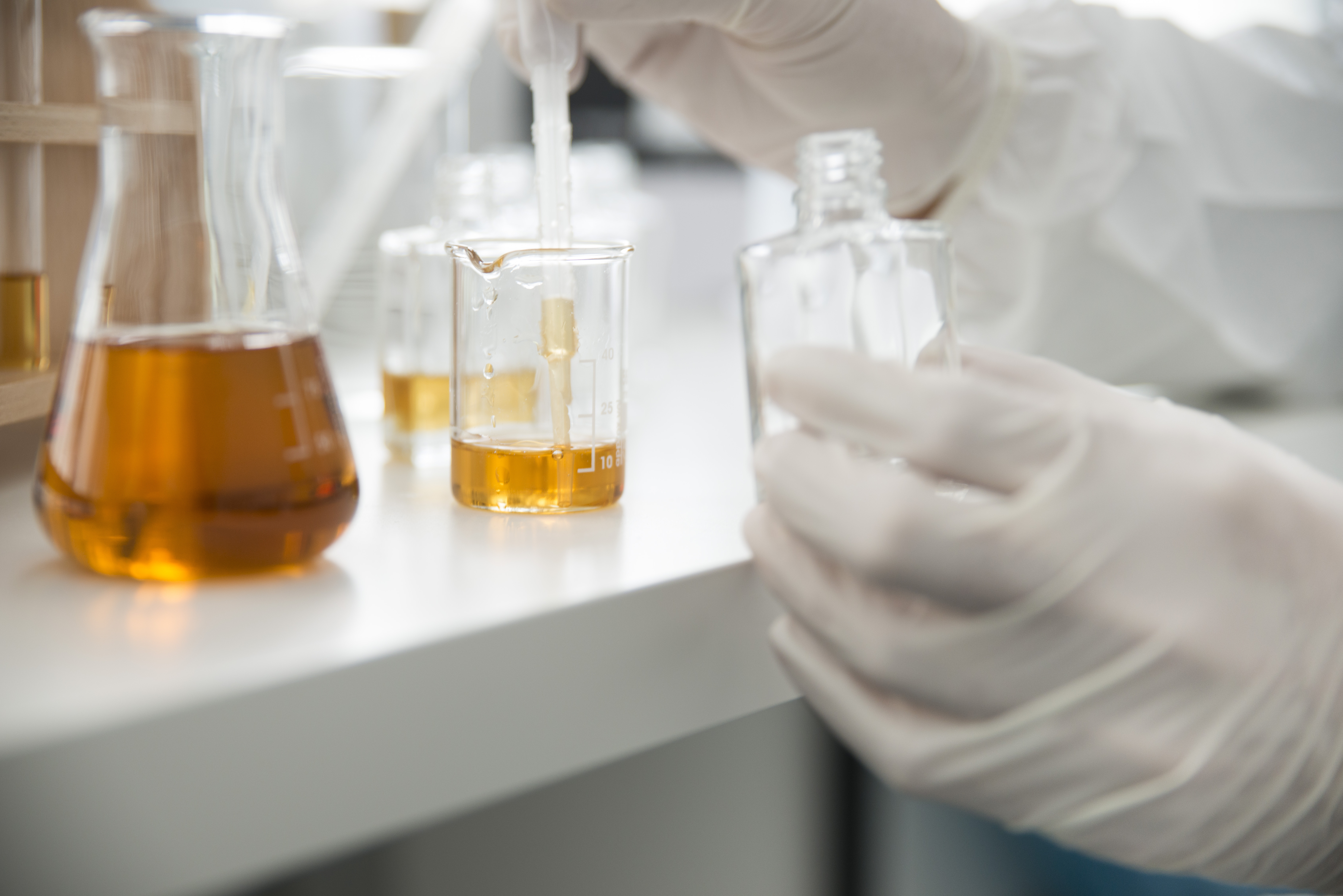 Lab / Laboratory closeup of hands in sterile gloves using a pipette to fill a glass bottle with liquid. 