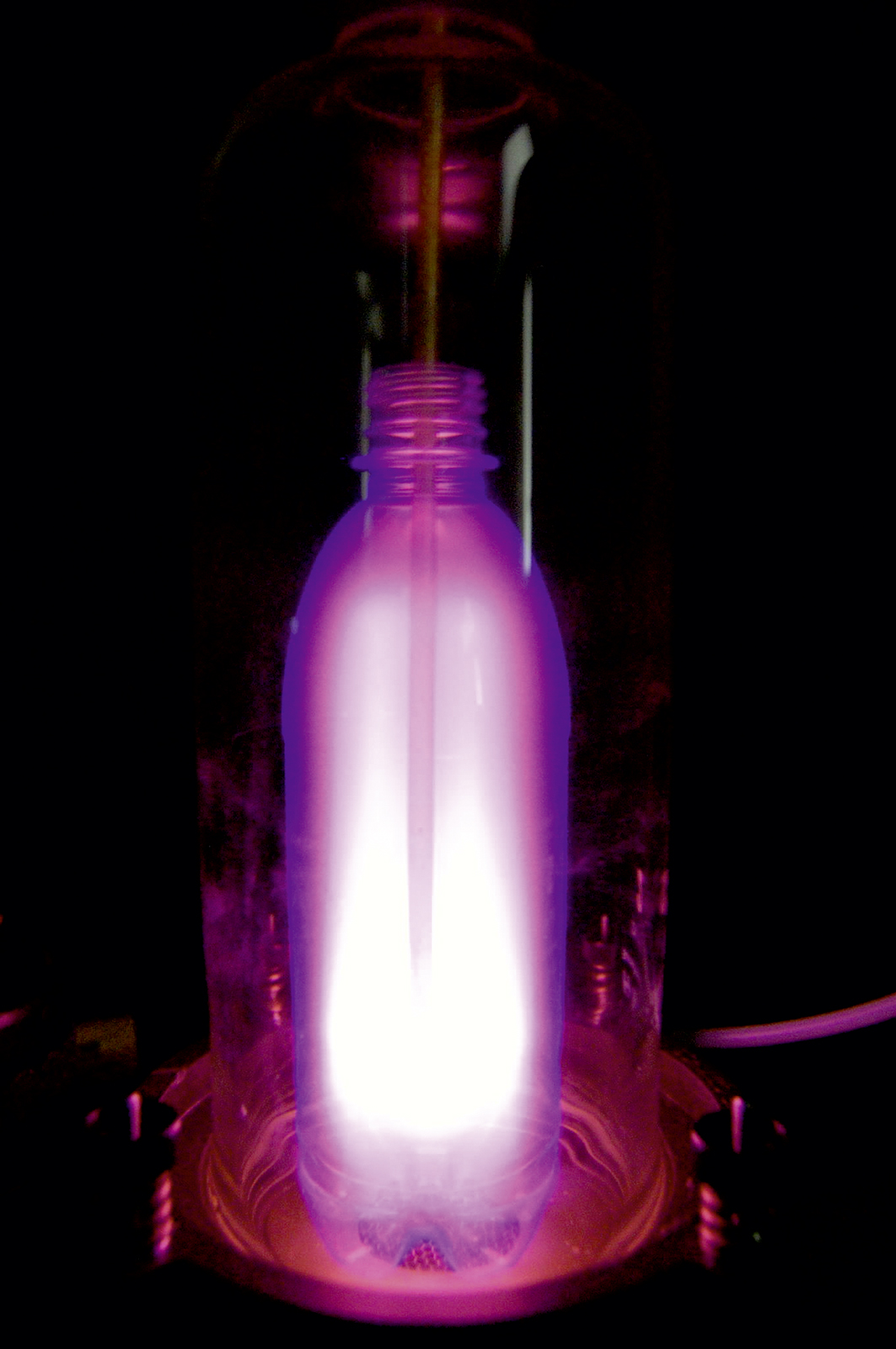 Beschichtung der Flascheninnenseite mittels Niederdruck-Plasma (pink leuchtend).
