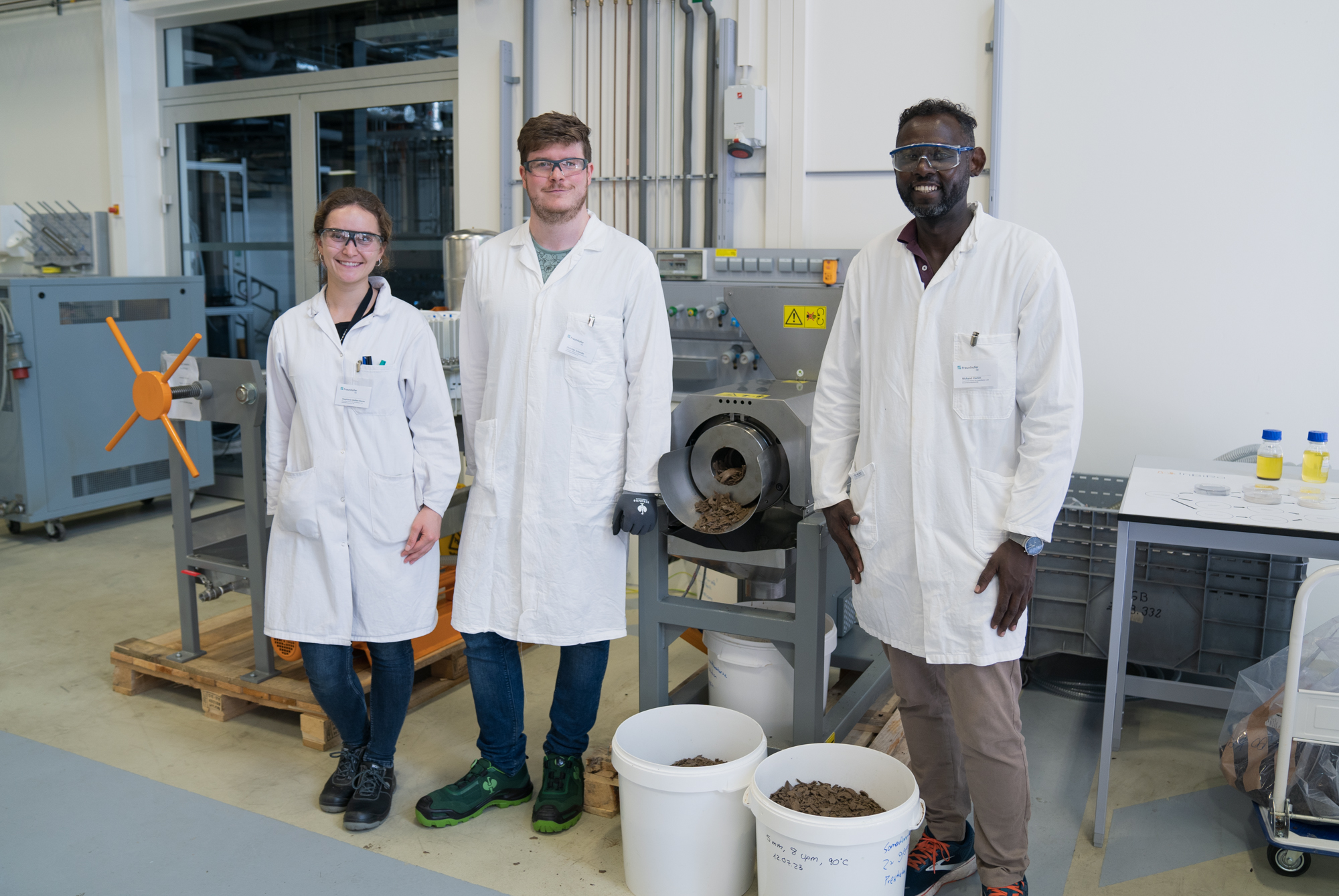 Drei Wissenschaftler vor einer Anlage zur Verarbeitung von getrockneten Insektenlarven